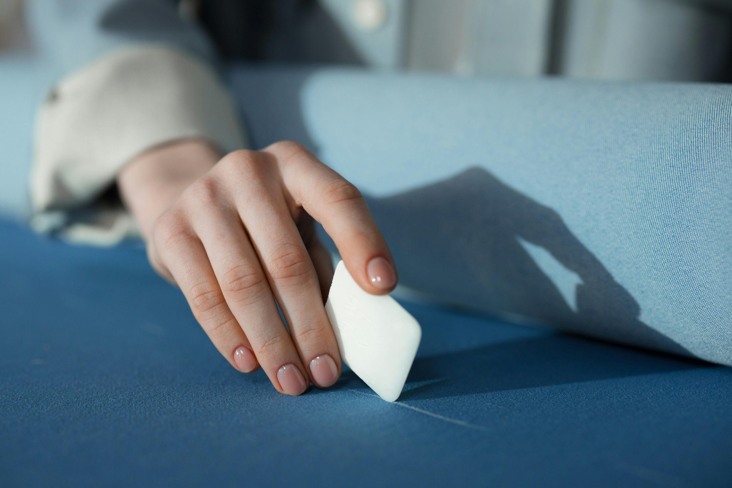 A detailed close-up of a person's hand using tailor's chalk on blue fabric in a sewing setting.